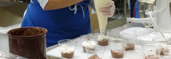 Piping whipped cream into pudding cups Piping whipped cream into pudding cups